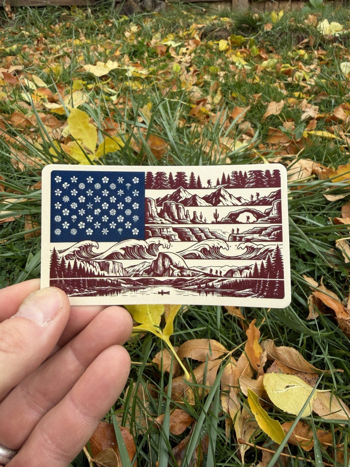 American Nature Flag sticker held in hand over fall leaves