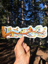A hand holds a birding wrap around sticker, die cut sticker wrap featuring a colorful illustration of various birds perched on tree branches with autumn leaves, set against a blurred forest background.