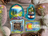 Four Colorado mountain, camping, wildflower and state-sign stickers on rustic wood