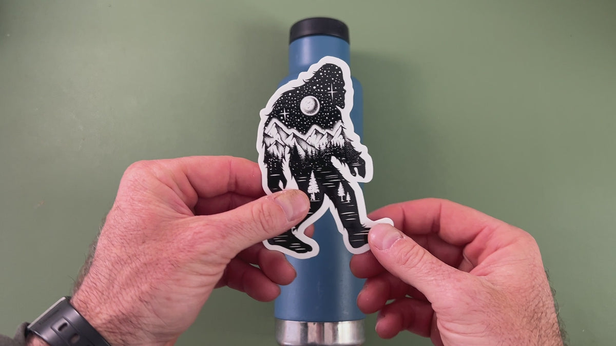 Applying a black-and-white Bigfoot sticker from the pack to a water bottle