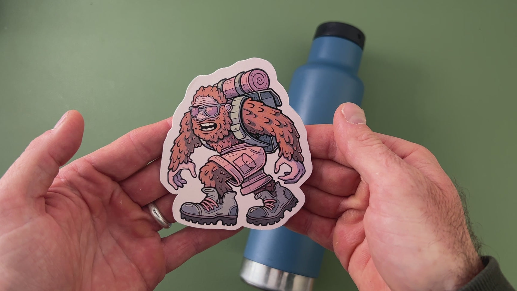 applying Sasquatch camping sticker to blue water bottle
