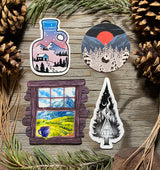 Four cozy mountain cabin and winter forest stickers displayed on rustic wood